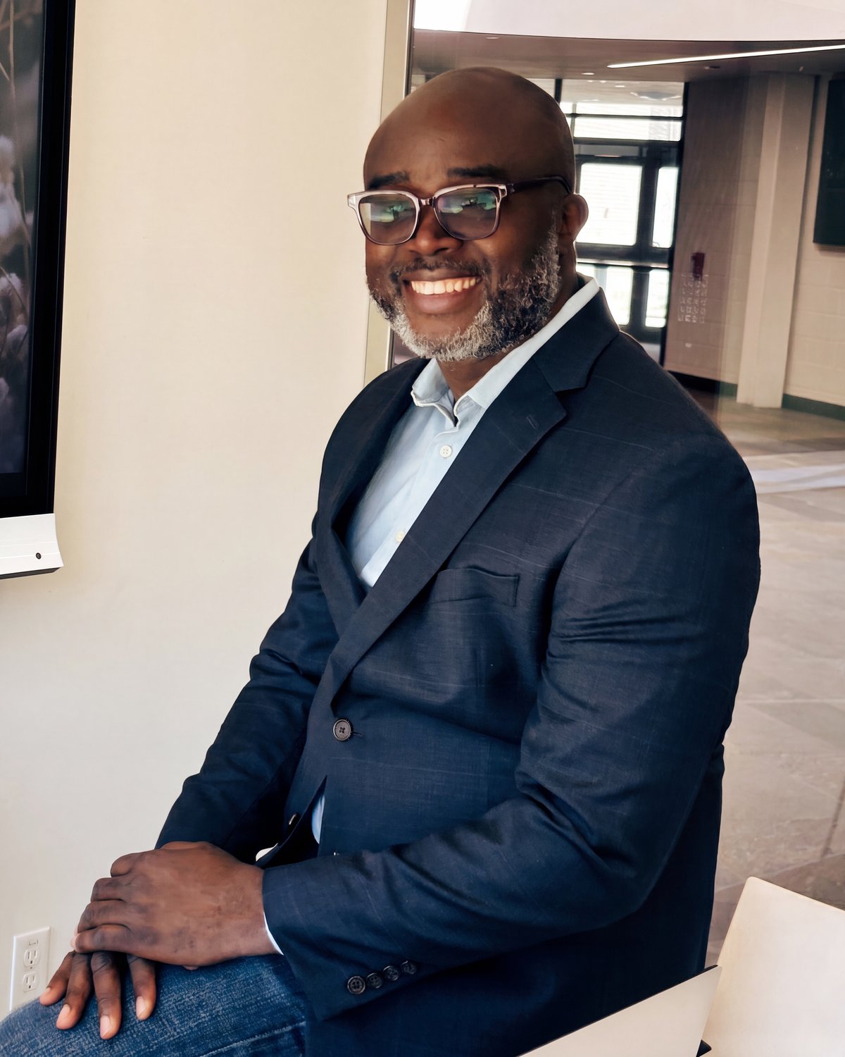 Gideon Adedokun seated in a navy blazer, smiling